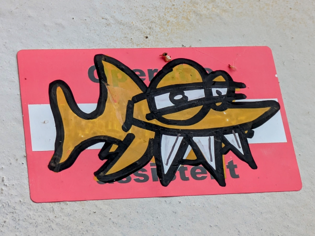 An orange graffiti fish with three teeth drawn on a sticker