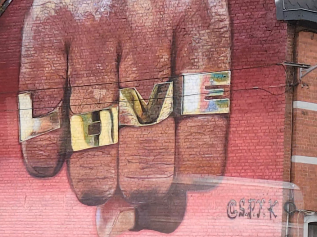 A large wall mural of a fist with LOVE letter rings across the knuckles